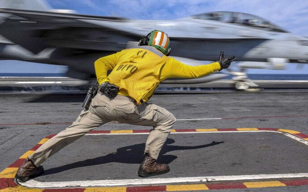 Carrier flight-deck launch officer signalling a fighter into the catapult — sortie generation