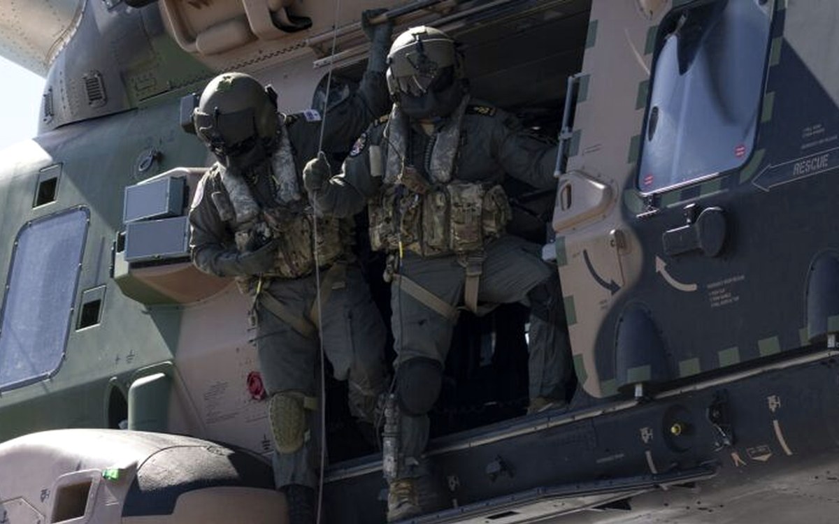 Aircrew in the door of a rotary-wing airframe showing rescue markings and structural detail